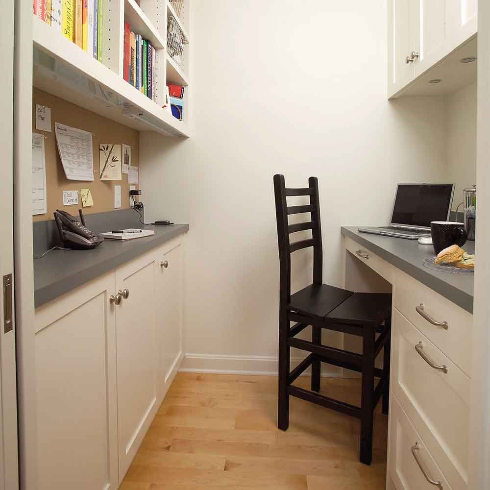 A black chair stands at a small desk with a laptop, in a cozy nook surrounded by shelves and a bulletin board, creating a workspace.