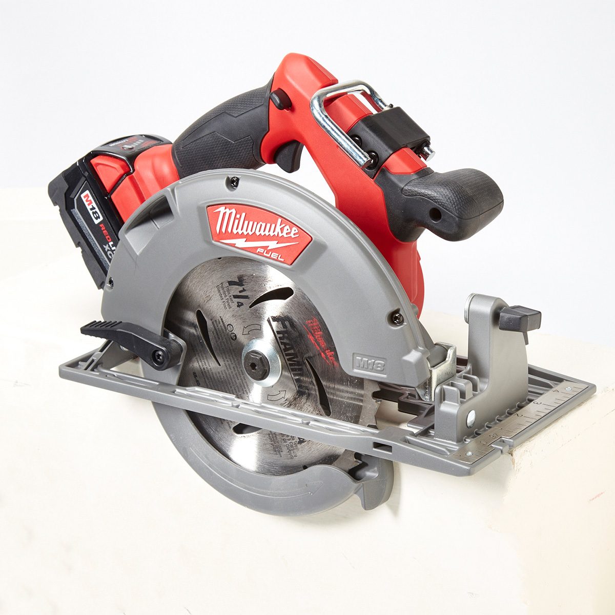 A cordless circular saw sits on a white surface, with a sharp blade exposed, ready for cutting materials. The handle is ergonomically designed for grip.