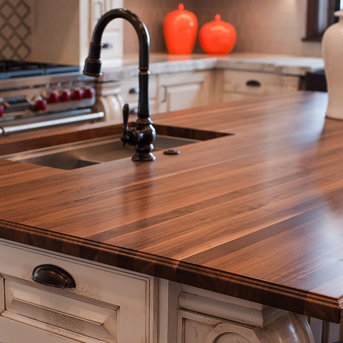 A polished wooden kitchen countertop features a black faucet above a sink, with orange decorative vases in the background, creating a warm, inviting atmosphere.