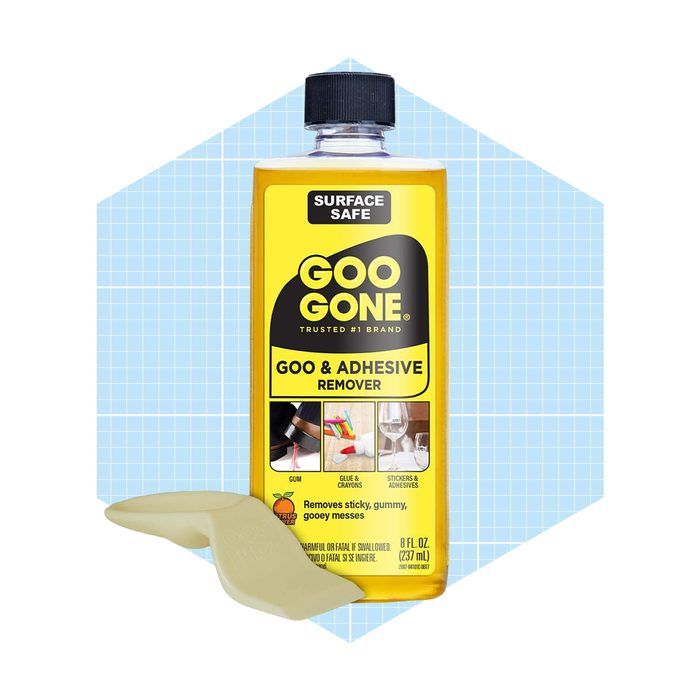 A yellow bottle of Goo Gone sits on a light blue grid background, with a cap and a complementary tool for applying the adhesive remover.