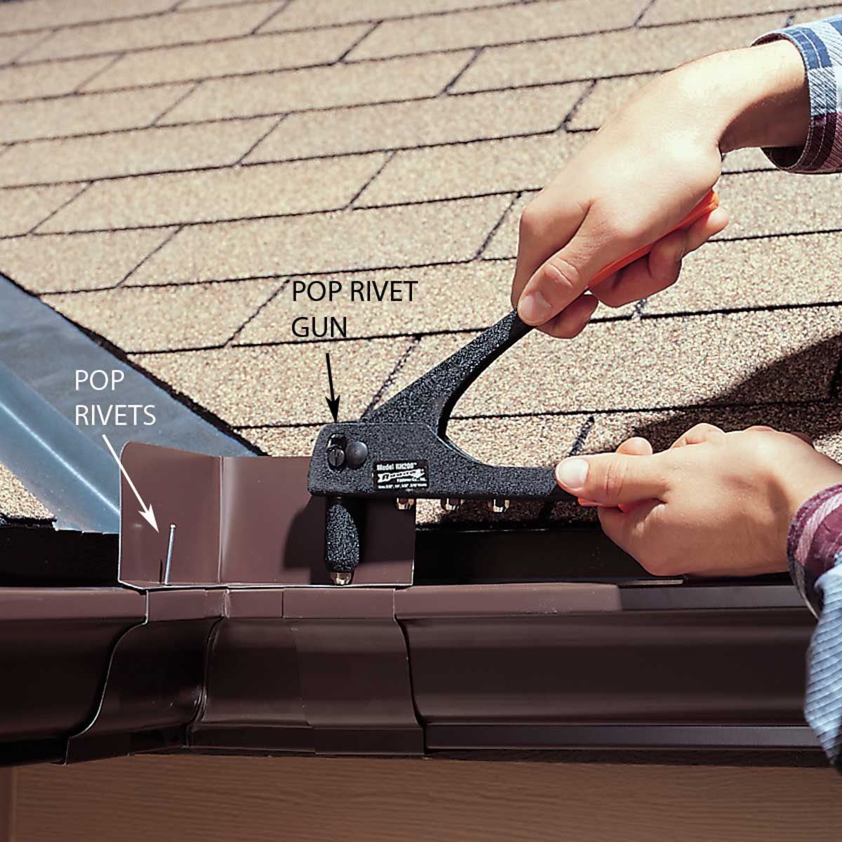 A person uses a pop rivet gun to secure metal pieces along a sloped roof covered with shingles, ensuring proper installation of gutters.