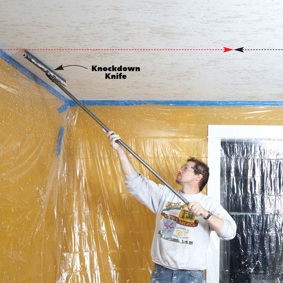 A person uses a long-handled tool to apply a texture to a ceiling in a room covered with plastic sheeting, with taped edges along the walls.