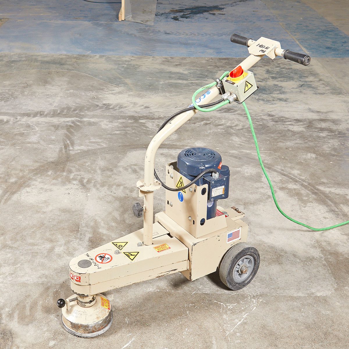 A floor grinder sits on a concrete surface, with its motor and controls visible. It appears ready for operation in a construction environment.