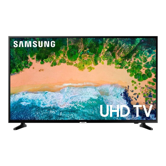 A television displays an aerial view of a beach, featuring vibrant green trees, sandy shore, and blue ocean waves, labeled 