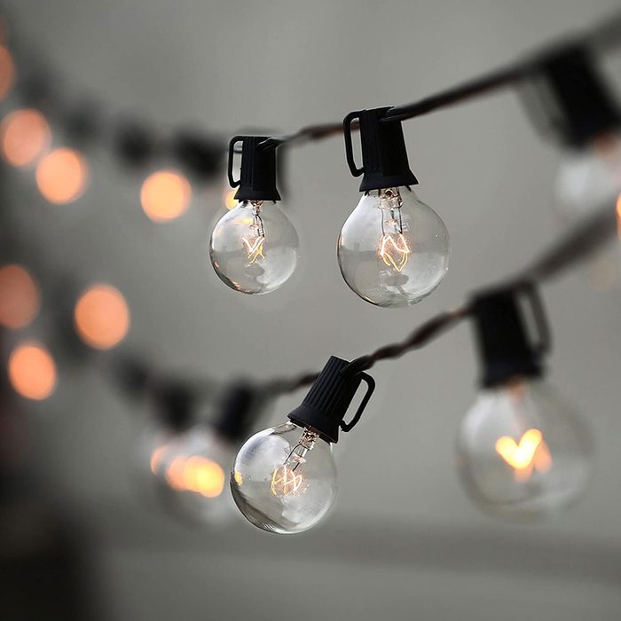 String lights hang from a cord, emitting a warm glow against a neutral background, creating a cozy atmosphere. The bulbs are round with visible filaments.