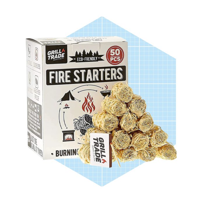 A box of eco-friendly fire starters sits next to a stacked pile of round, straw-like materials, set against a light blue geometric background.