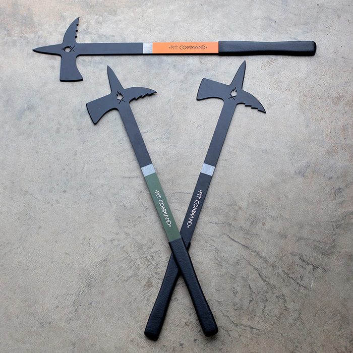 Three black throwing tools, each with sharp points, rest on a smooth, gray surface. Two are labeled with green and orange bands, respectively.