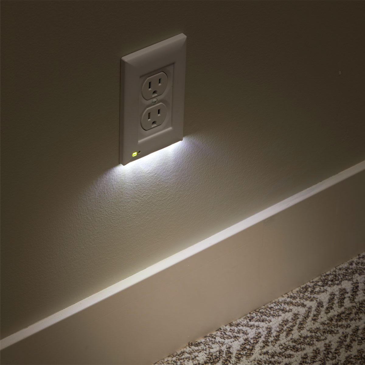 A wall outlet emits a soft light, illuminating the area around it, against a plain wall and carpet, providing low-level lighting.
