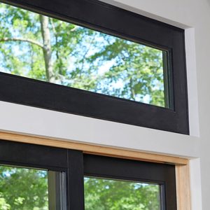 A large window with a black frame reflects greenery outside, allowing natural light to fill a modern interior space with light-colored walls.