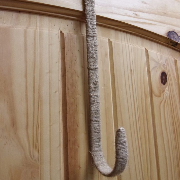 A wrapped hook hangs vertically on a wooden surface, showcasing light-colored planks with noticeable grain patterns and knots.