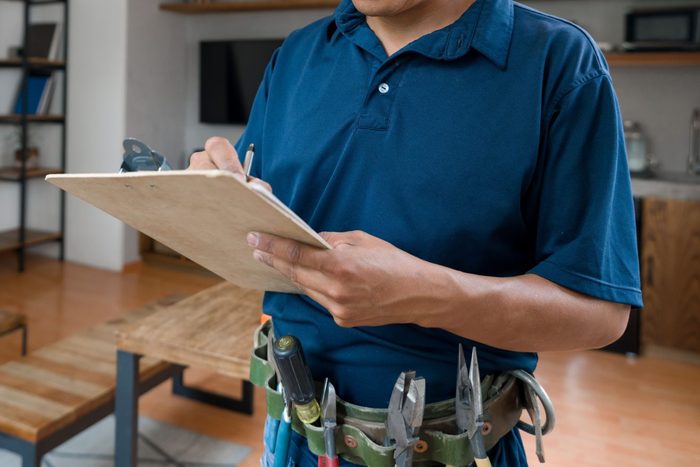 Electrician working at a house and writing a report on a clipboard