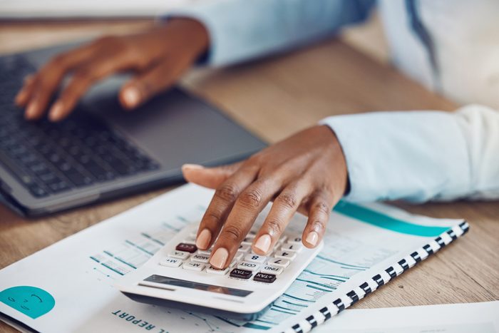 Calculator, accounting and financial accountant with finance documents to check sales revenue of the company in an office. Data analysis, inflation and African employee working on budget spreadsheet