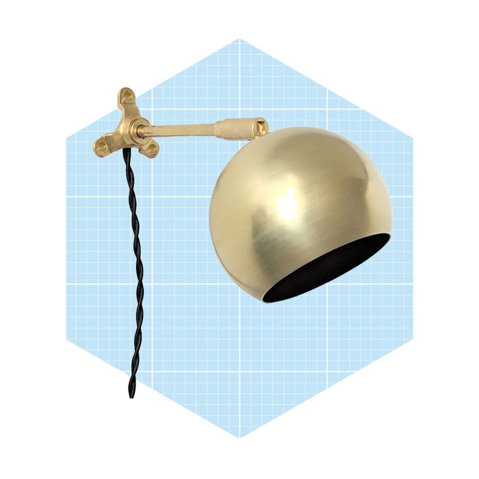 A modern wall lamp with a metallic round shade is mounted on an arm, featuring a twisted black cord against a light blue grid background.