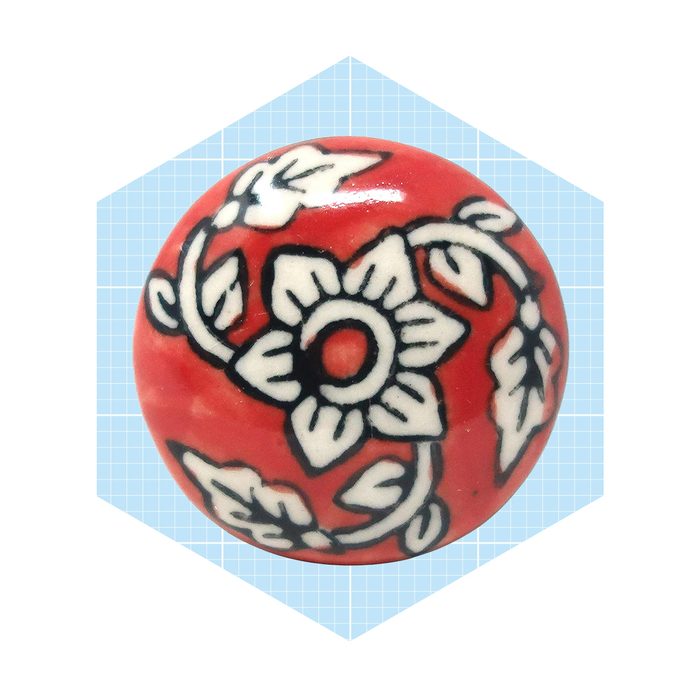 A round, red decorative ball features intricate white floral and leaf patterns, set against a light blue grid background.